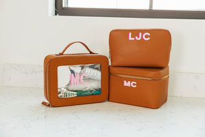 A collection of tan leather toiletry bags are customized with matching pink monograms.