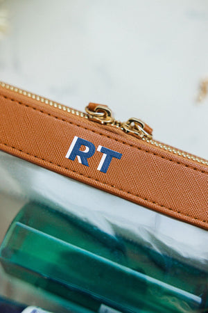 A tan leather case is personalized with a navy and white monogram.