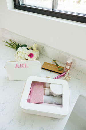 A white leather toiletry case is placed in a bathroom filled with toiletries.