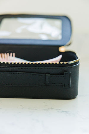 A black leather toiletry case is laid open showing off it's gold zipper and adjustable handle.