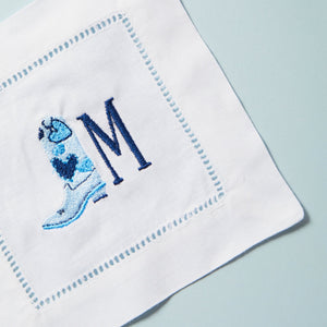 An embroidered cocktail napkin with a cowboy boot and initial.