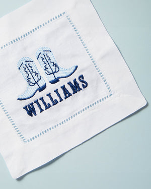 An embroidered cocktail napkin with cowboy boots and last name