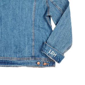 A jean jacket sleeve lies face up to show the custom initial printed onto the sleeve.