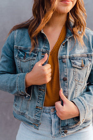 A person wears a jean jacket with "Laine" written on it in a white font.