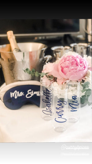 Custom script champagne flutes are set out onto a table with custom sleep masks and an ice bucket for a wedding party.