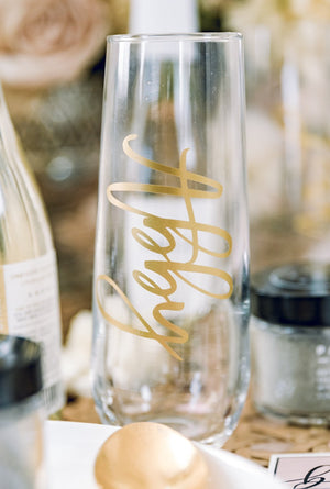 A champagne flute which is customized with a gold script name, "Abby"