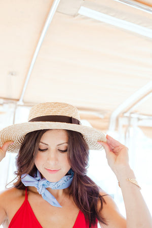 A woman in a beach hat shows off her light blue custom bandana around her neck.