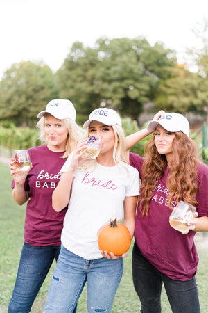 A group of girls drink out of monogrammed wine glasses and wear custom hats and t shirts