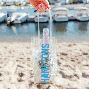 A person holds their wine bag customized with "Hamptons" in blue writing up at a marina.