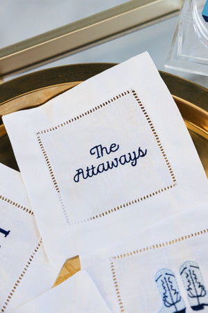A cocktail napkin that is embroidered in navy font with a custom last name.
