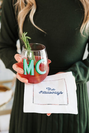 A woman holds a cocktail napkins under her drinks which is embroidered with a custom last name.