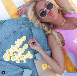 A woman lays next to a custom retro jean jacket with white and yellow shadow text.