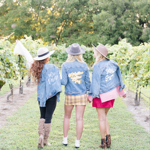 Three women walk down a vineyard wearing matching custom jean jackets.