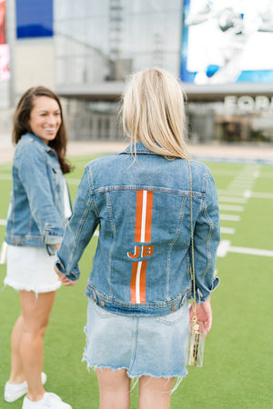 Two women walking on a field sport their striped monogram jean jackets.