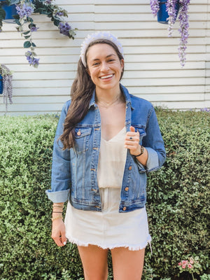 A woman in a headband stands outside showing off the fit of her custom jean jacket.