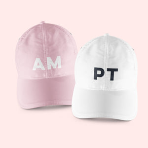 A pink and a white baseball hat are customized with block initials.
