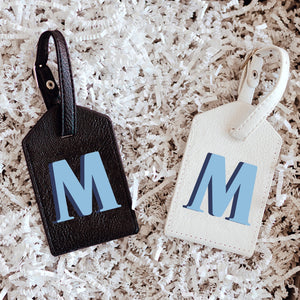 Two luggage tags one black and one white with a blue "M" on the front