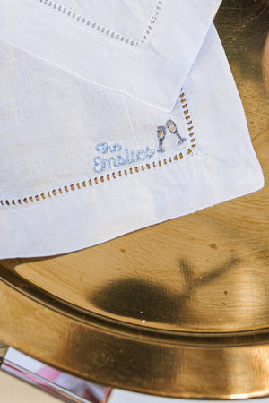 An embroidered cocktail napkin with a last name and two wine glass motifs.