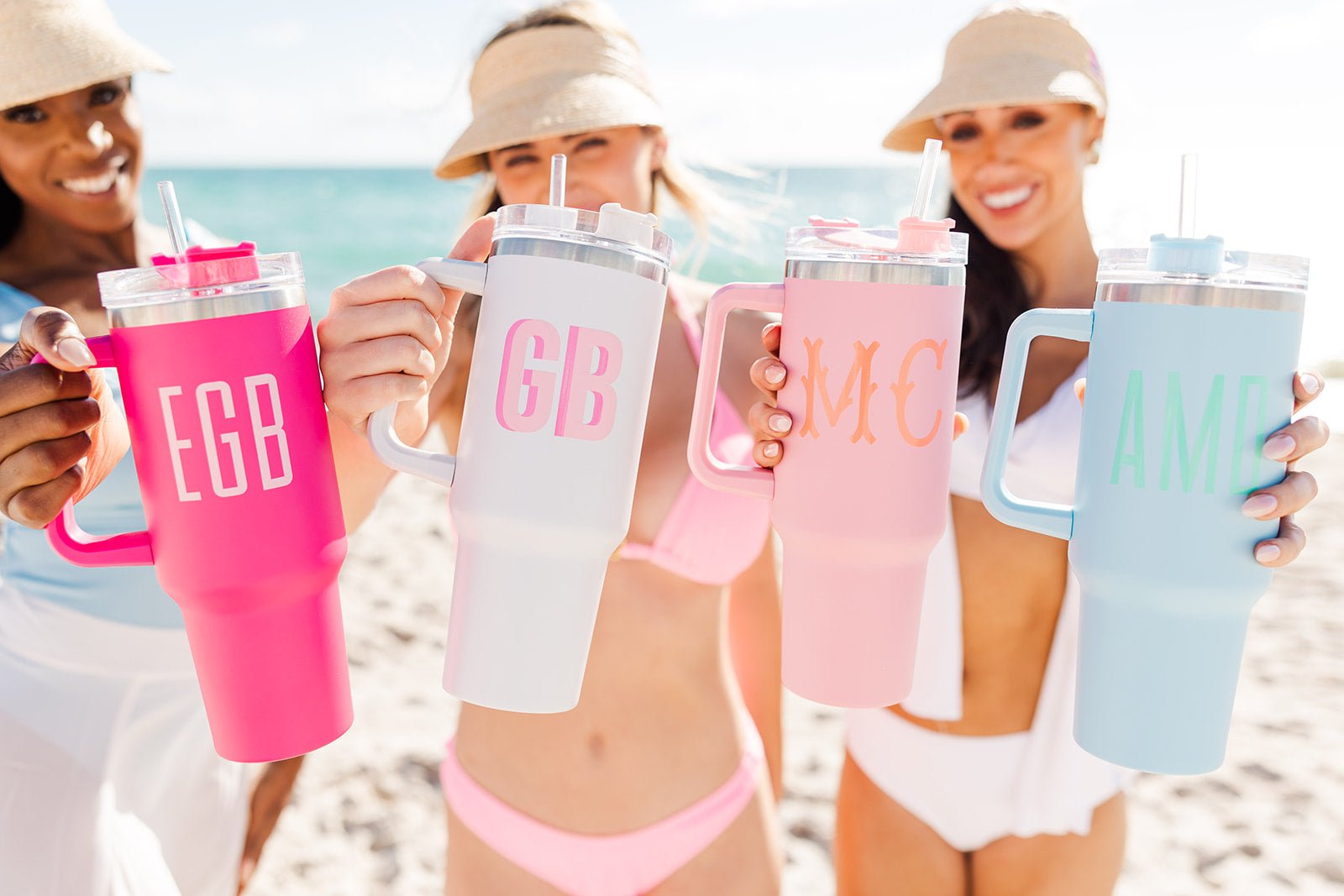 Three monogrammed tumblers with handles in pink, white, and blue