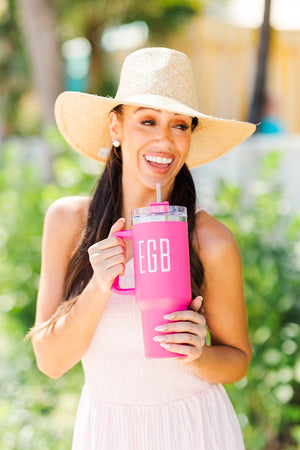 A woman wearing summer clothes holds a hot pink, monogrammed tumbler