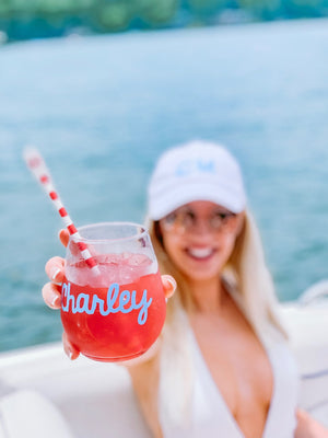 A woman on a lake holds up her customized wine glass with her name in light blue. 