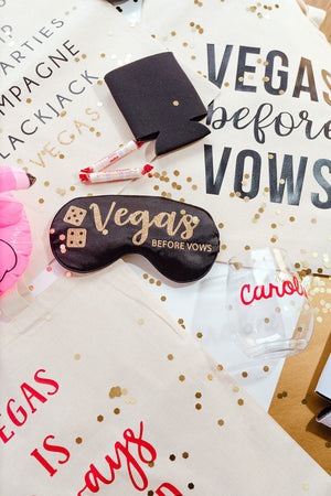 A black sleep mask which reads "Vegas Before Vows" is laid with various other Vegas themed products.