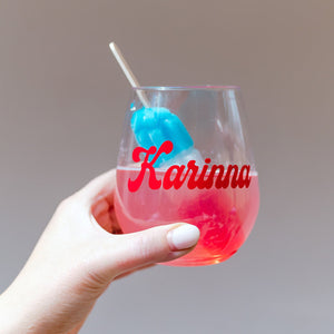 A stemless wine glass with a popsicle is held up to show off the personalization of their name in red.