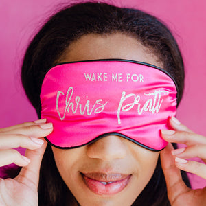 A woman wears a pink customized sleep mask which reads "Wake me for Chis Pratt"