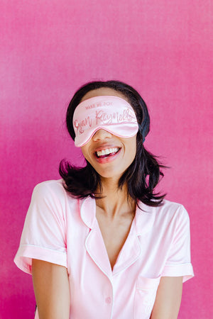 A woman wears a pink customized sleep mask which reads "Wake me for Ryan Reynolds"