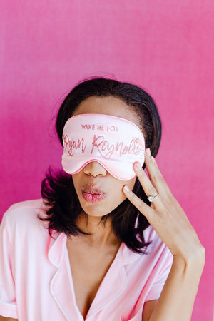 A woman wears a pink customized sleep mask which reads "Wake me for Ryan Reynolds"