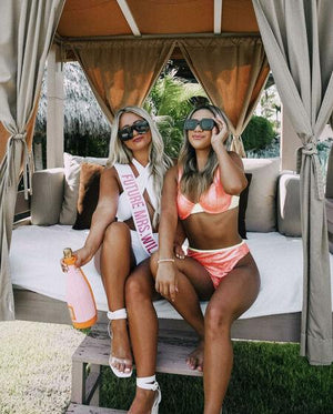 Two women sit in a cabana one is wearing a "Future Mrs." sash