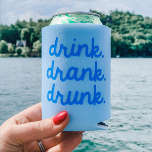 A person holds up a light blue koozie which reads drink drank drunk in a dark blue font.