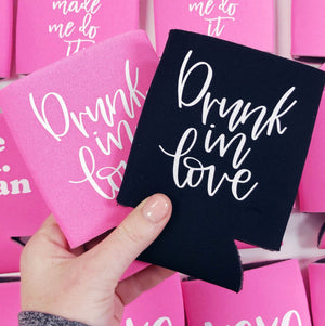 A person holds a black and pink koozie which both read "Drunk in love" in a white script font.