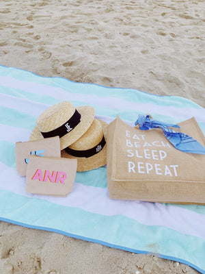 An assortment of products lays on the beach on a blue beach towel.