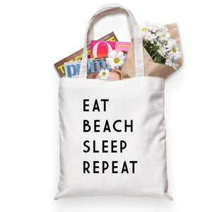 A "Eat Sleep Beach Repeat" tote holds a bouquet of flowers and some magazines.