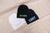 Three embroidered beanies sit on a pile they are navy, black, and white