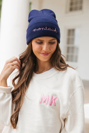 A brunette wears an embroidered beanie and monogrammed corded sweatshirt