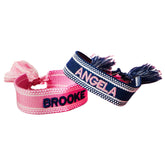 A pink bracelet and a blue bracelet are customized with embroidered names.