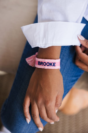 A woman shows off her light pink bracelet which is customized with her name in a navy thread color.