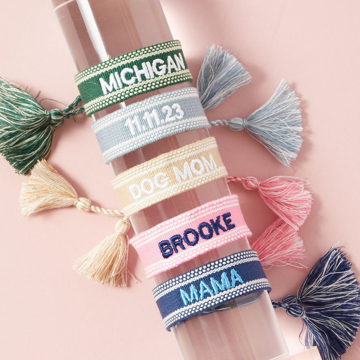 Three colorful bracelets are stacked showing off their custom embroidered text.