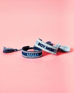 A blue bracelet and a light blue bracelet are stacked in front of a pink background showing off their embroidered customizations which read "Mama" and "Boy Mom."