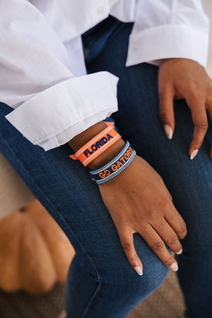 A woman wears an orange bracelet which reads "Florida" in navy thread and a blue bracelet which reads "Go Gators" in orange thread to show off her school pride.