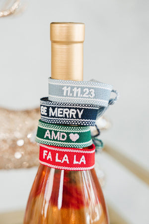 A stack of bracelets sits on top of a wine bottle showing off some of the options that could be embroidered on a custom bracelet.