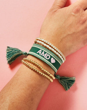 A woman shows off her wrist which has a green bracelet that is embroidered with her initials and a heart motif in a light pink thread.