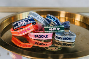 A stack of bracelets is laid out to show off some of the embroidered text that could be used to customize this bracelet