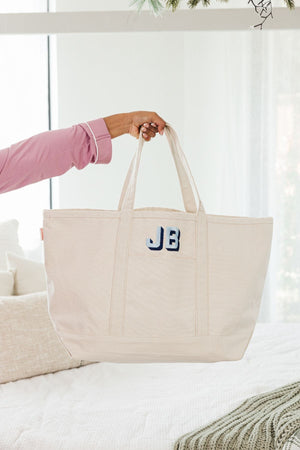A girl holds up a natural colored canvas tote with a blue block monogram.