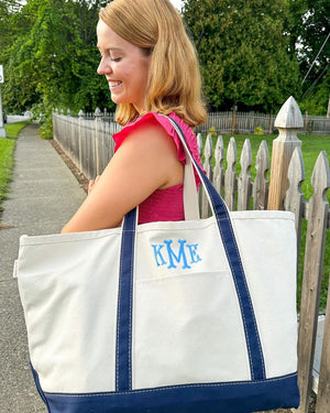A female in a pink dress carries a monogrammed canvas tote with blue coloring