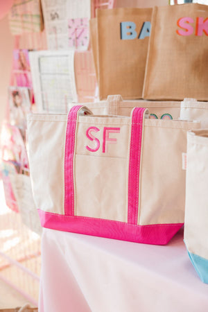A pink and white canvas tote with pink initials embroidered on it