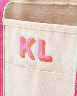 A pink and orange monogram is embroidered into a pink canvas tote.
