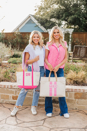 Two girls stand outside showing off their pink monogrammed totes